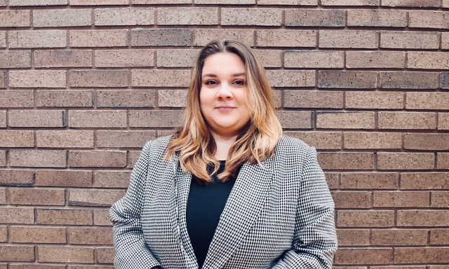 Person in a houndstooth blazer standing in front of a brick wall.