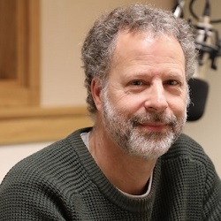 Eric Zolov Man with facial hair, wearing a sweater, sits in front of a large microphone